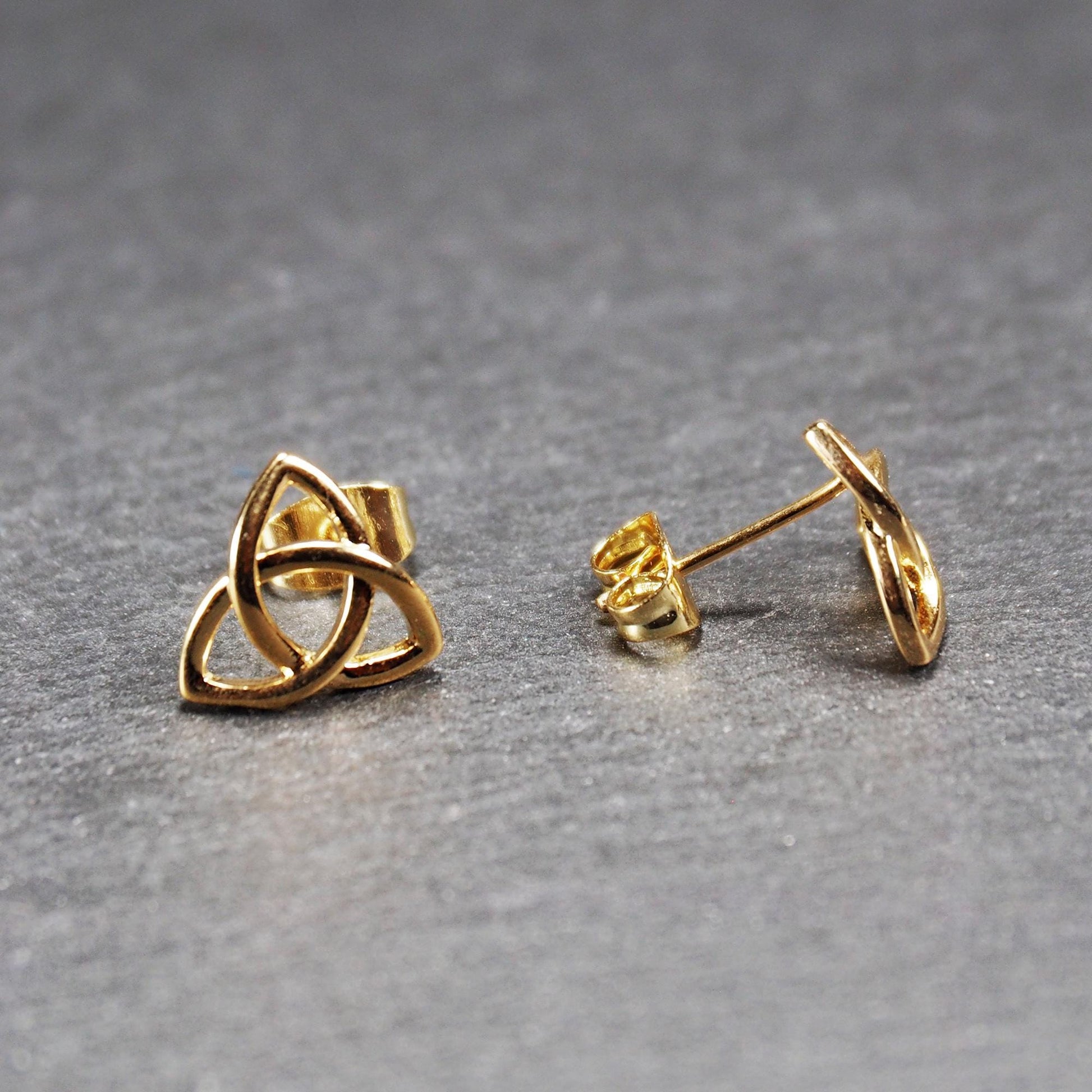 Paar goldfarbener Ohrstecker mit offen gearbeitetem Triquetra-Knoten, glänzende Oberfläche und sichtbaren Schmetterlingsverschlüssen.