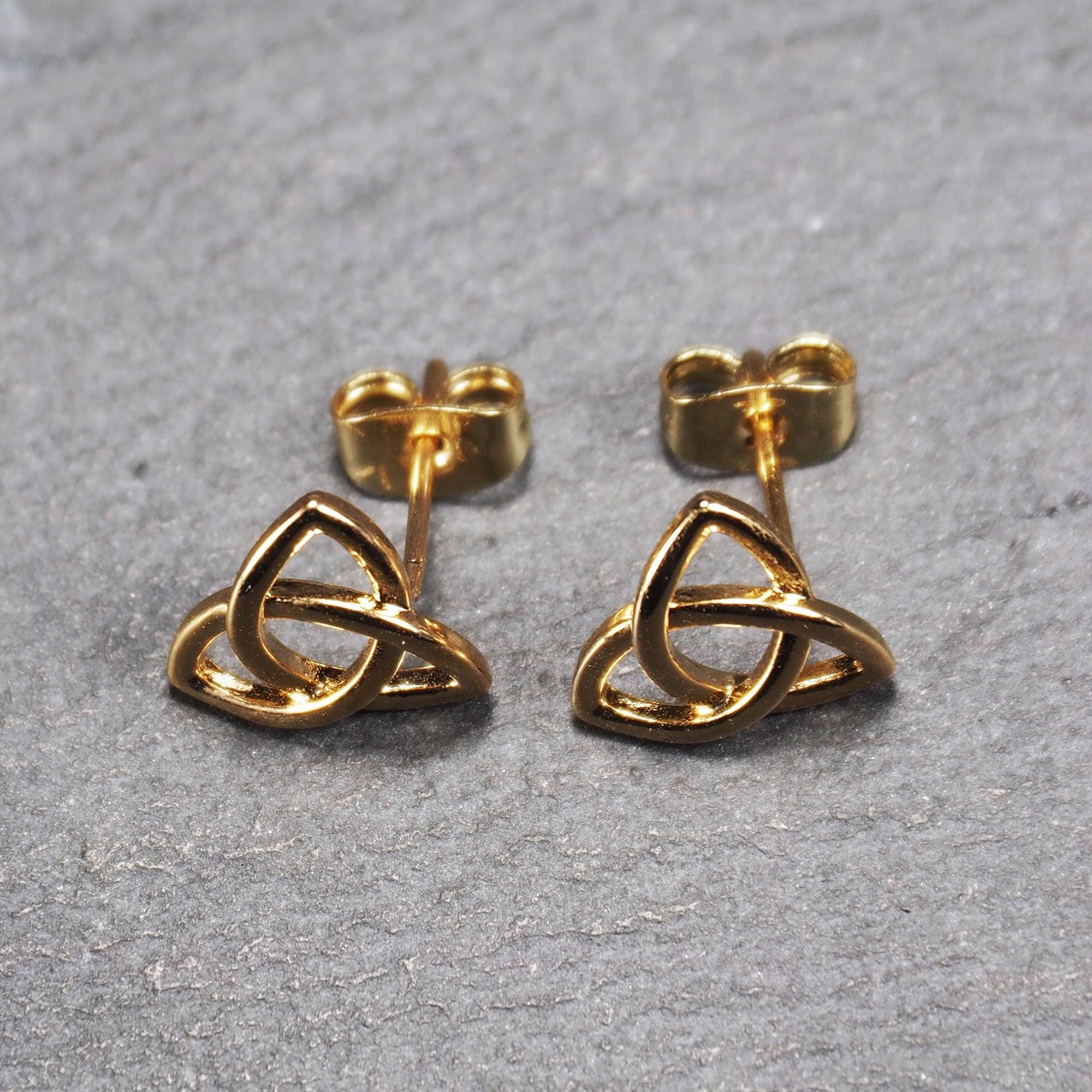 Paar goldfarbener Ohrstecker mit offen gearbeitetem Triquetra-Knoten, glänzende Oberfläche und sichtbaren Schmetterlingsverschlüssen.
