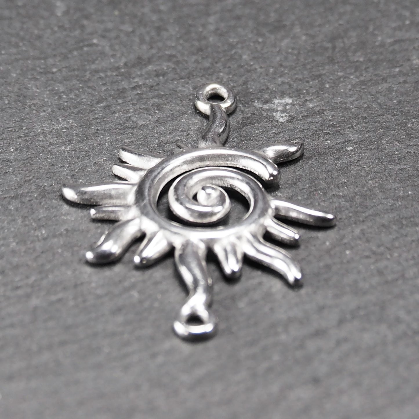 Sonnenförmiger silberner Verbinder mit glänzender Oberfläche, spiralförmigem Durchbruchzentrum, reliefartigen flammenförmigen Strahlen und zwei Ösen.