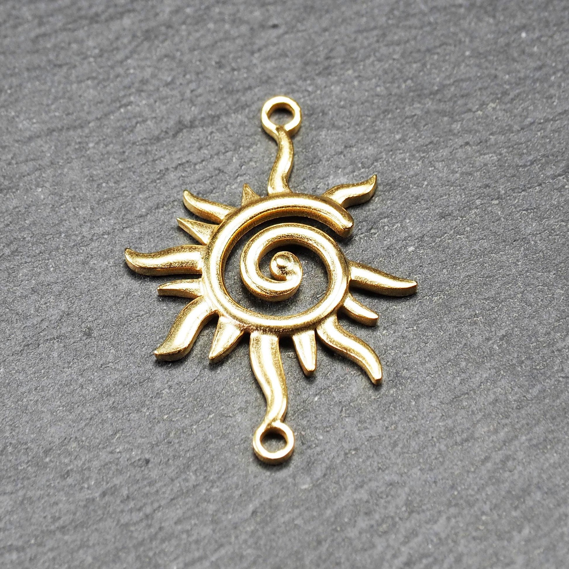 Goldfarbener, durchbrochener Sonnen-Verbinder mit spiralförmigem Zentrum, unregelmäßigen wellenförmigen Strahlen und je einer Öse oben und unten.