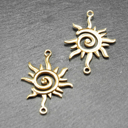 Goldfarbener, durchbrochener Sonnen-Verbinder mit spiralförmigem Zentrum, unregelmäßigen wellenförmigen Strahlen und je einer Öse oben und unten.  Vorder- und Rückseite.