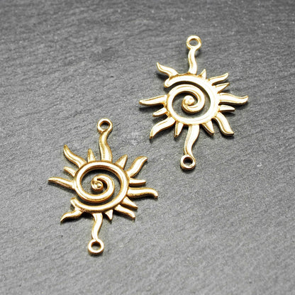 Goldfarbener, durchbrochener Sonnen-Verbinder mit spiralförmigem Zentrum, unregelmäßigen wellenförmigen Strahlen und je einer Öse oben und unten.  Vorder- und Rückseite.