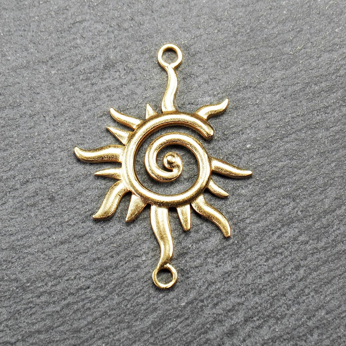 Goldfarbener, durchbrochener Sonnen-Verbinder mit spiralförmigem Zentrum, unregelmäßigen wellenförmigen Strahlen und je einer Öse oben und unten.