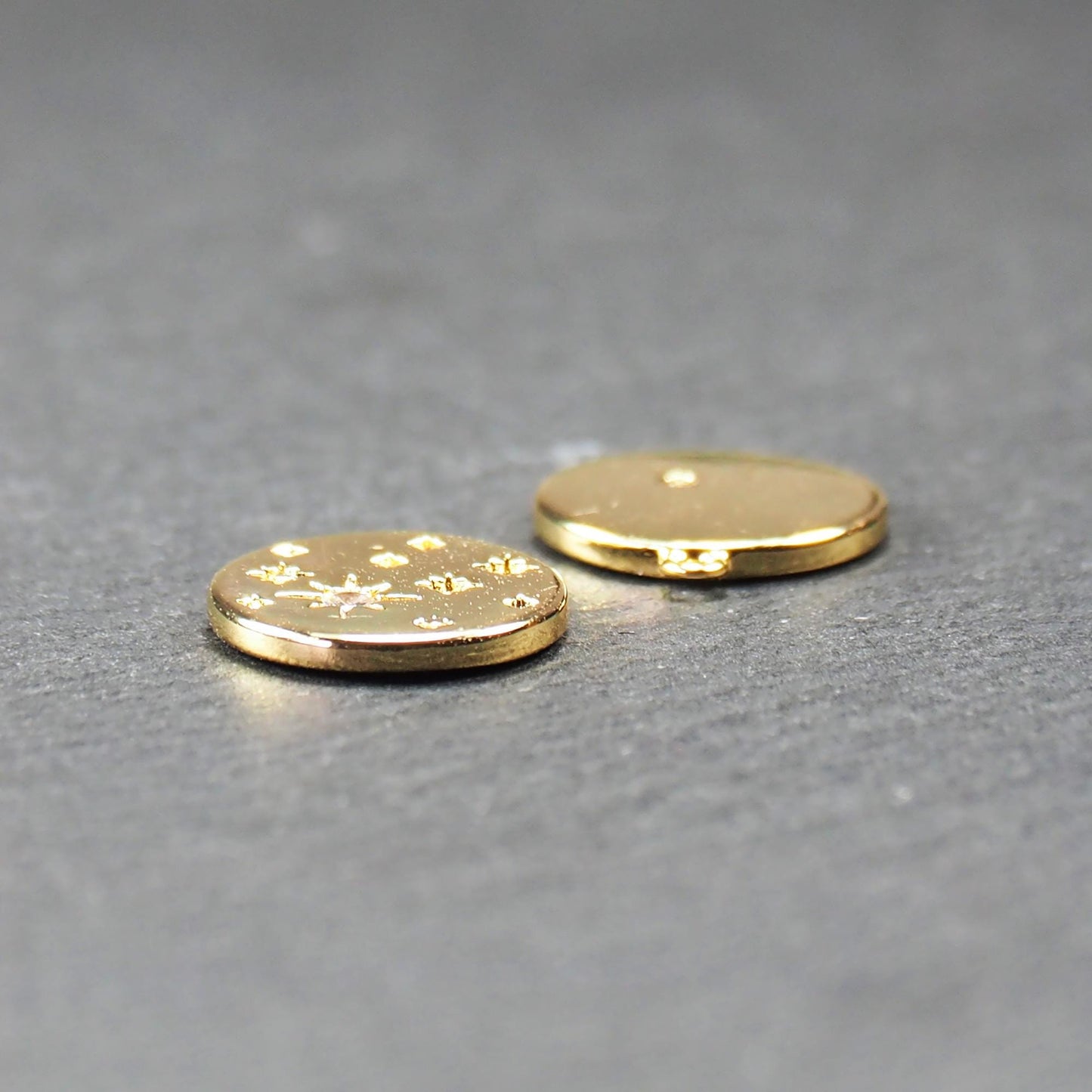 Runder goldfarbener Anhänger, glänzend glatt, mit reliefiertem Stern und mittigem klarem Stein, mehreren kleinen Sternen und oberer Öse. Vorder- und Rückseite.