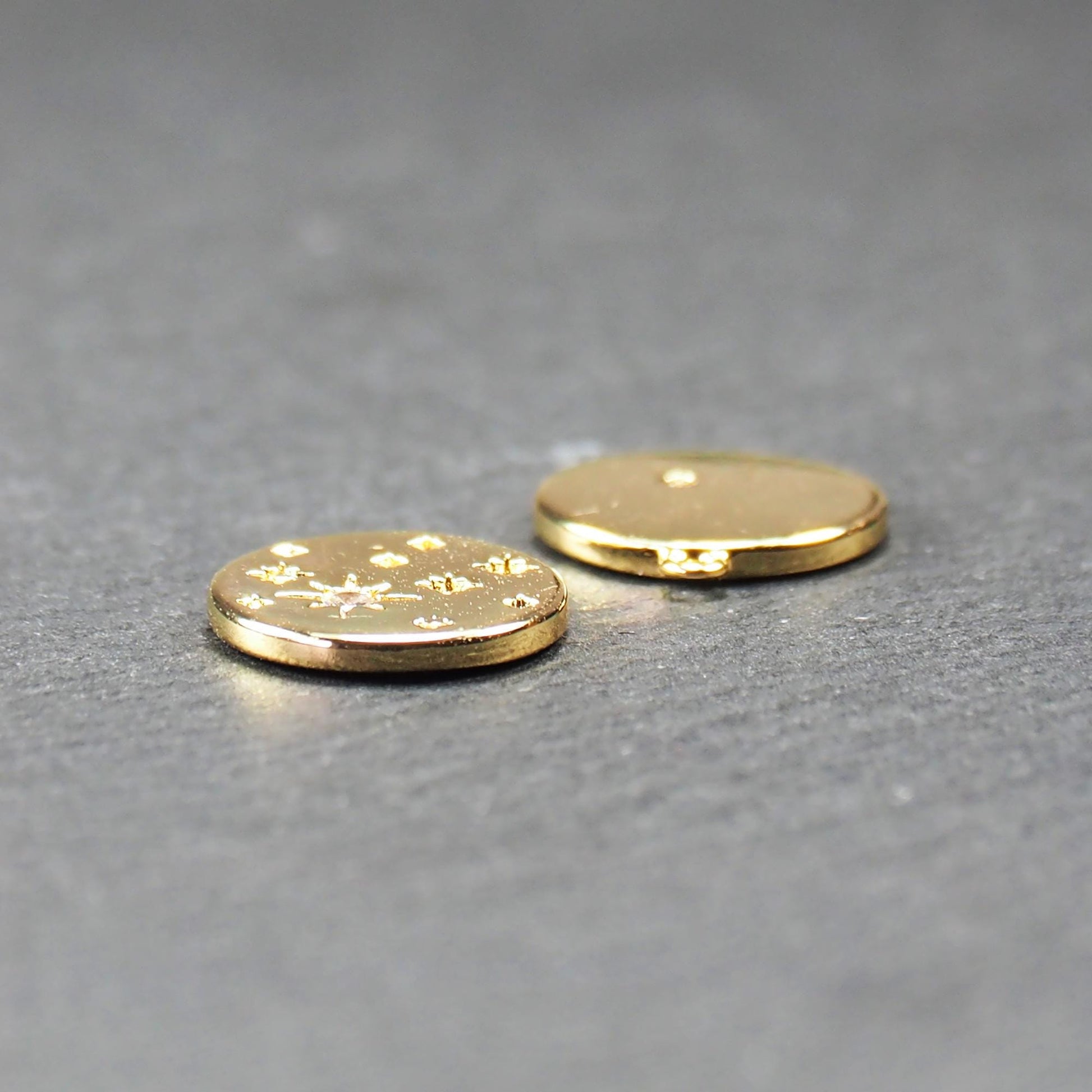 Runder goldfarbener Anhänger, glänzend glatt, mit reliefiertem Stern und mittigem klarem Stein, mehreren kleinen Sternen und oberer Öse. Vorder- und Rückseite.