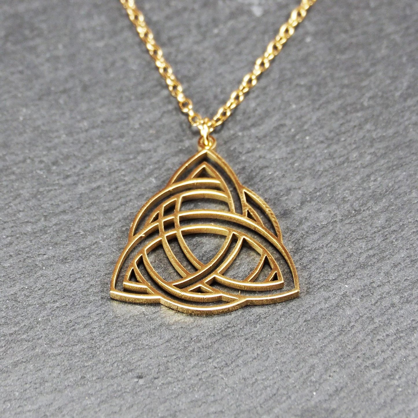 Vergoldeter Anhänger in offener Triquetra-Knotenform mit filigranen Durchbrüchen, an dünner goldfarbener Kette und sichtbarer Öse.