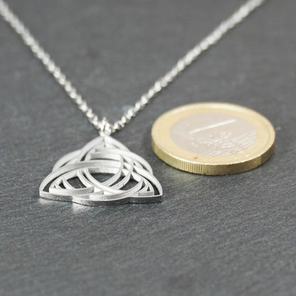 Anhänger, silberfarben glänzend; dreieckige, offene Triquetra-Knotenform mit filigraner Durchbruchstruktur und sichtbarer Öse an feiner Gliederkette. 1-Euro-Münze als Größenvergleich.