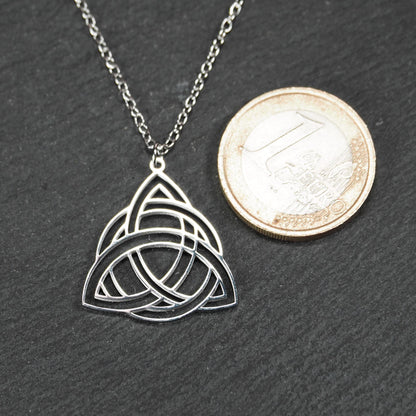 Anhänger, silberfarben glänzend; dreieckige, offene Triquetra-Knotenform mit filigraner Durchbruchstruktur und sichtbarer Öse an feiner Gliederkette. 1-Euro-Münze als Größenvergleich.