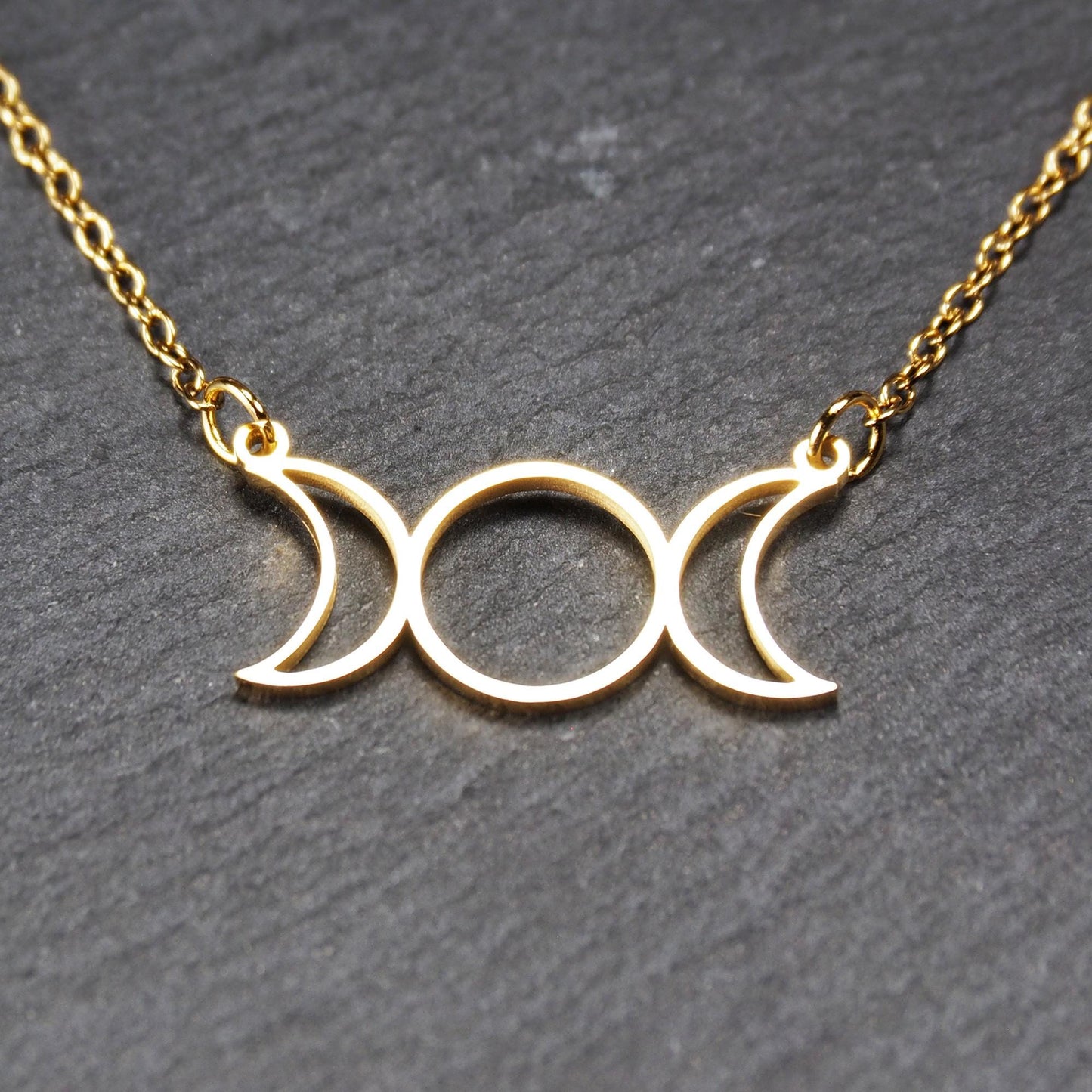 Collier mit goldfarbenem, offenem Anhänger in dreifacher Mondform (Mondsichel-Kreis-Mondsichel), an einer feinen Gliederkette mittels Ösen befestigt.