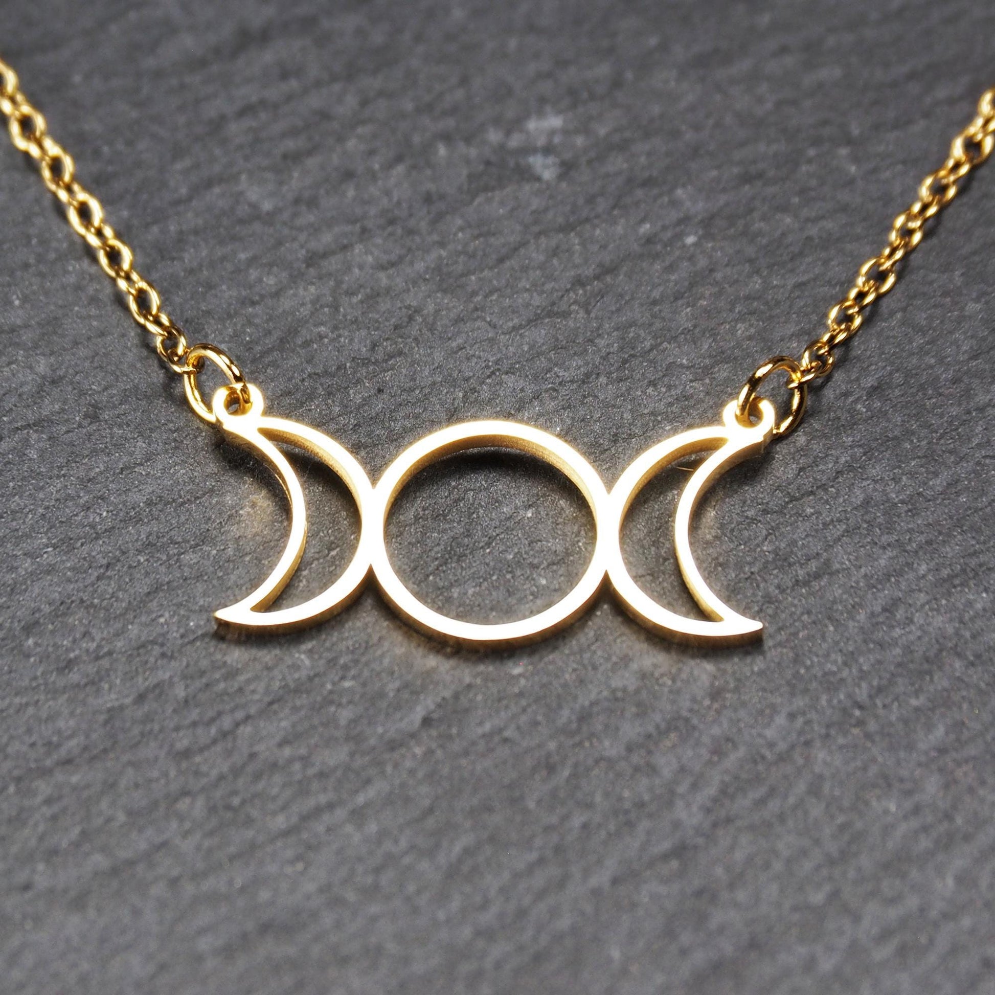 Collier mit goldfarbenem, offenem Anhänger in dreifacher Mondform (Mondsichel-Kreis-Mondsichel), an einer feinen Gliederkette mittels Ösen befestigt.