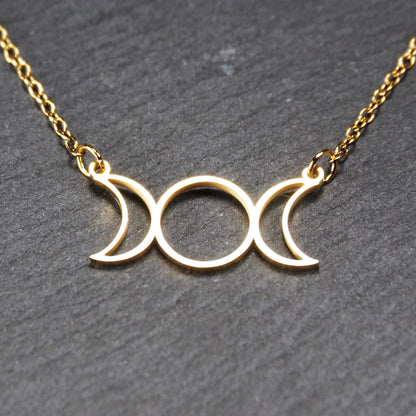Collier mit goldfarbenem, offenem Anhänger in dreifacher Mondform (Mondsichel-Kreis-Mondsichel), an einer feinen Gliederkette mittels Ösen befestigt.