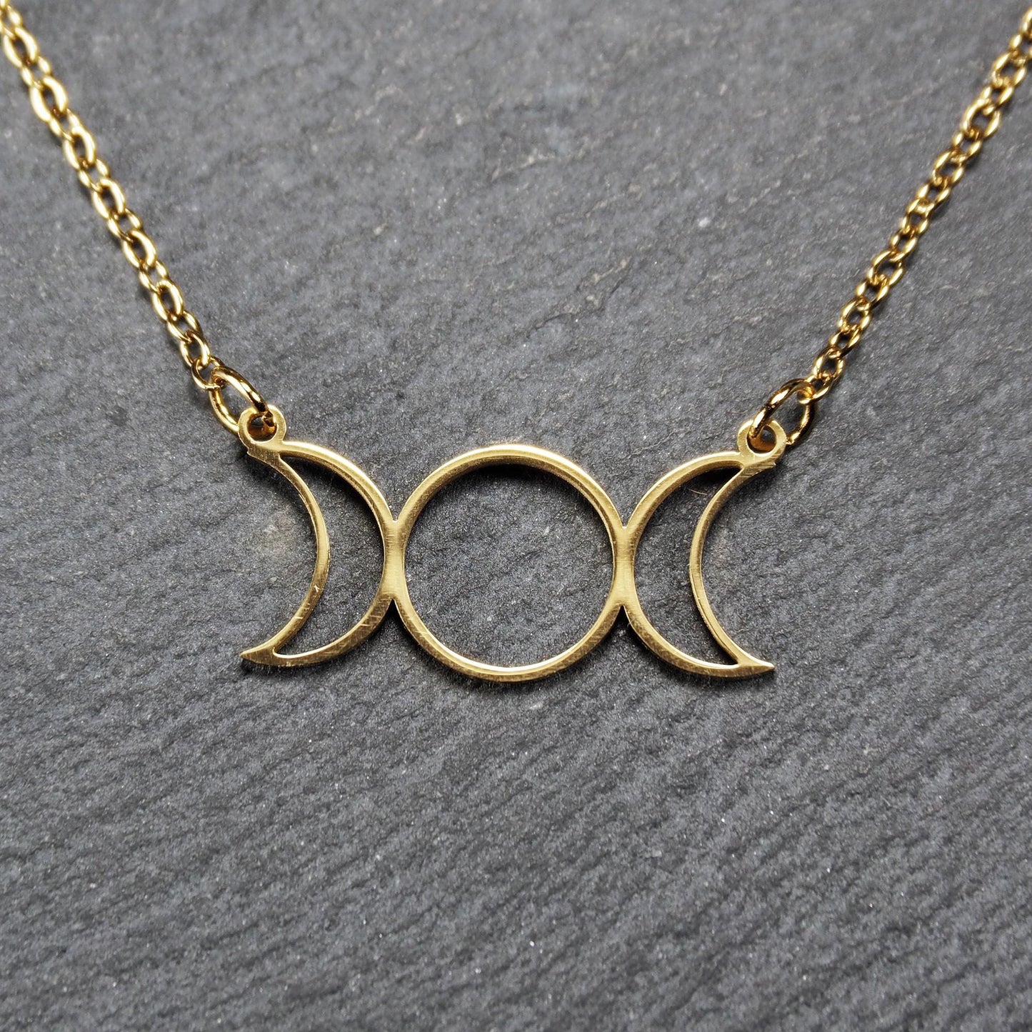 Collier mit goldfarbenem, offenem Anhänger in dreifacher Mondform (Mondsichel-Kreis-Mondsichel), an einer feinen Gliederkette mittels Ösen befestigt.