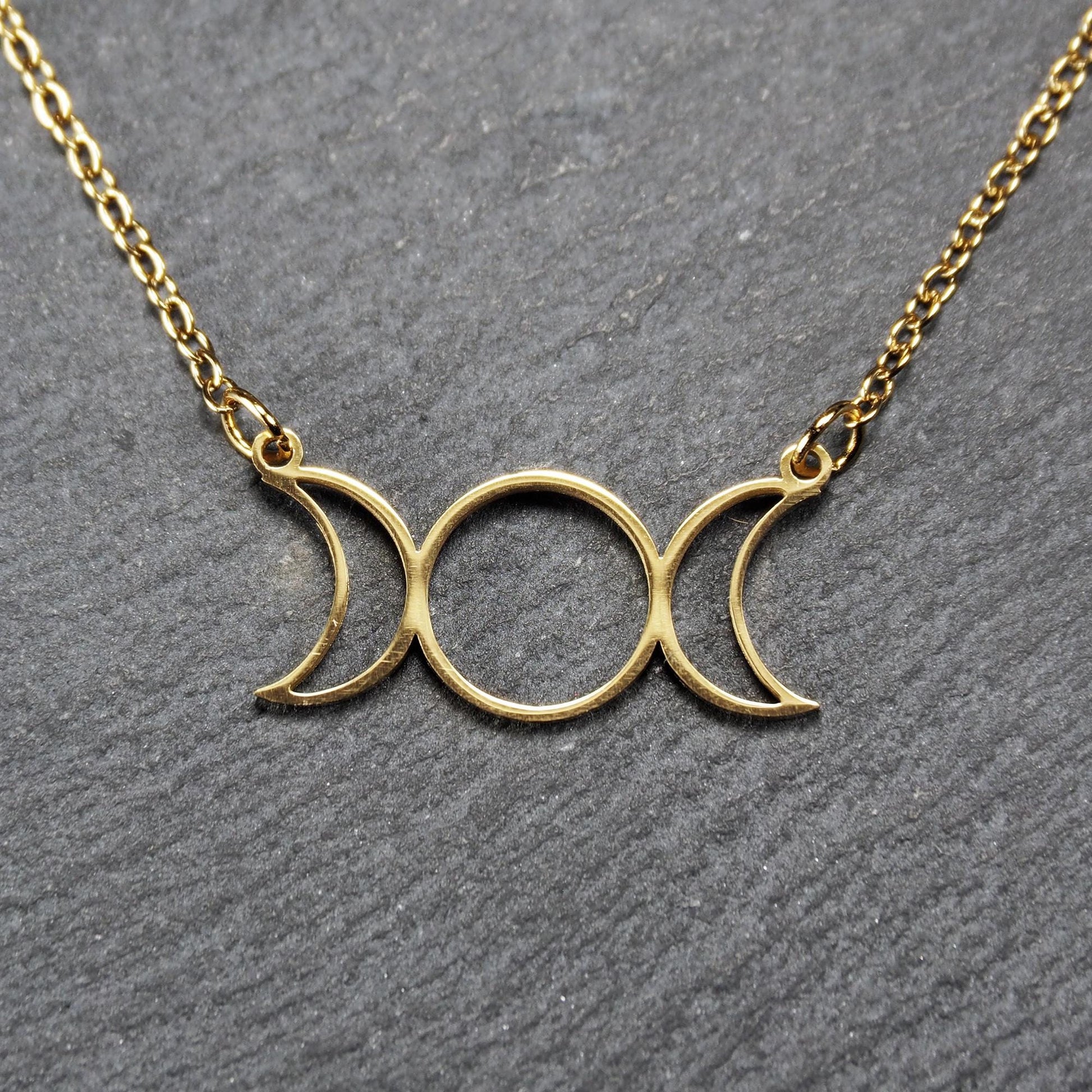 Collier mit goldfarbenem, offenem Anhänger in dreifacher Mondform (Mondsichel-Kreis-Mondsichel), an einer feinen Gliederkette mittels Ösen befestigt.