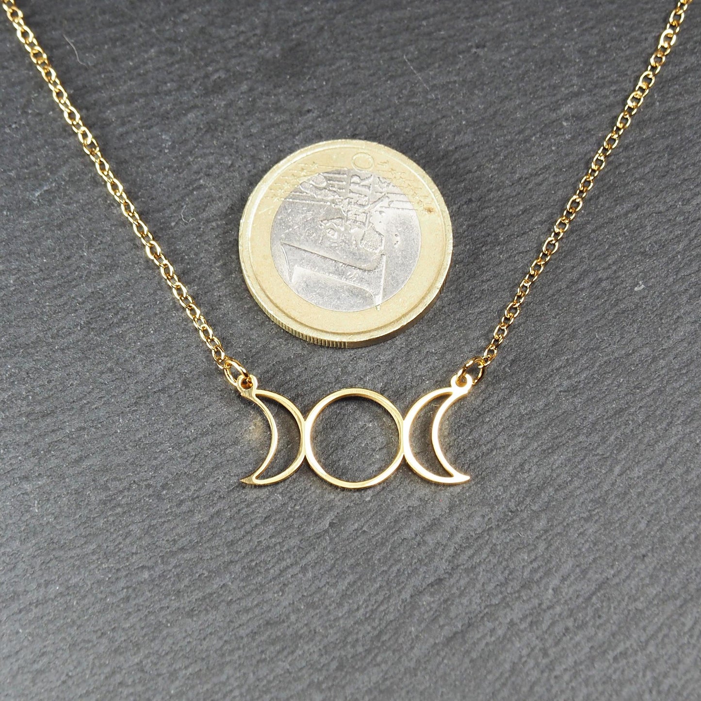 Collier mit goldfarbener Kette und offenem, durchbrochenem Anhänger in Form der dreifachen Mondgöttin mit Ösen; Ein-Euro-Münze als Größenvergleich.