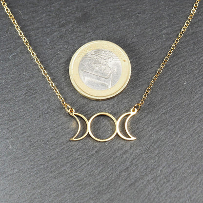 Collier mit goldfarbener Kette und offenem, durchbrochenem Anhänger in Form der dreifachen Mondgöttin mit Ösen; Ein-Euro-Münze als Größenvergleich.