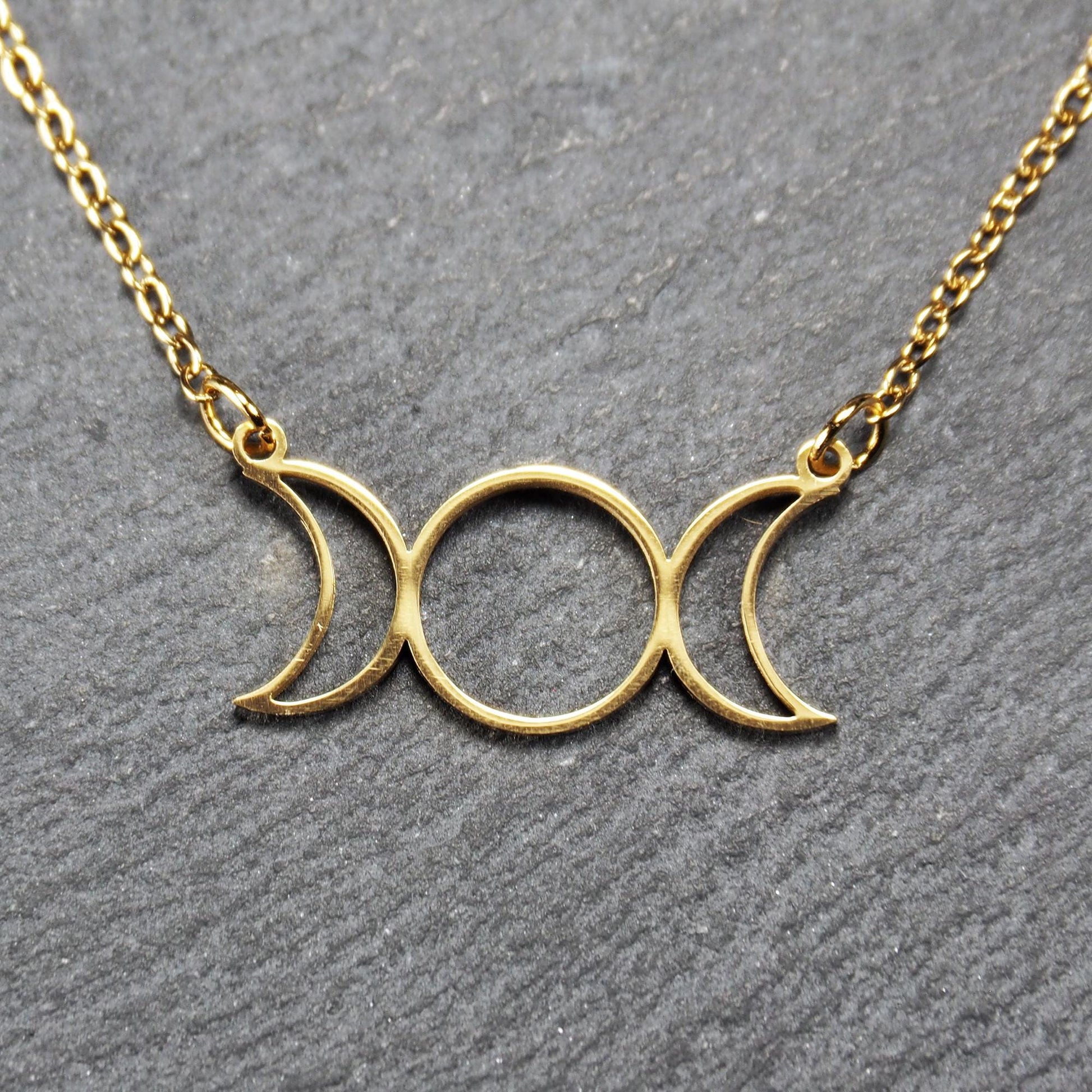Collier mit goldfarbenem, offenem Anhänger in dreifacher Mondform (Mondsichel-Kreis-Mondsichel), an einer feinen Gliederkette mittels Ösen befestigt.