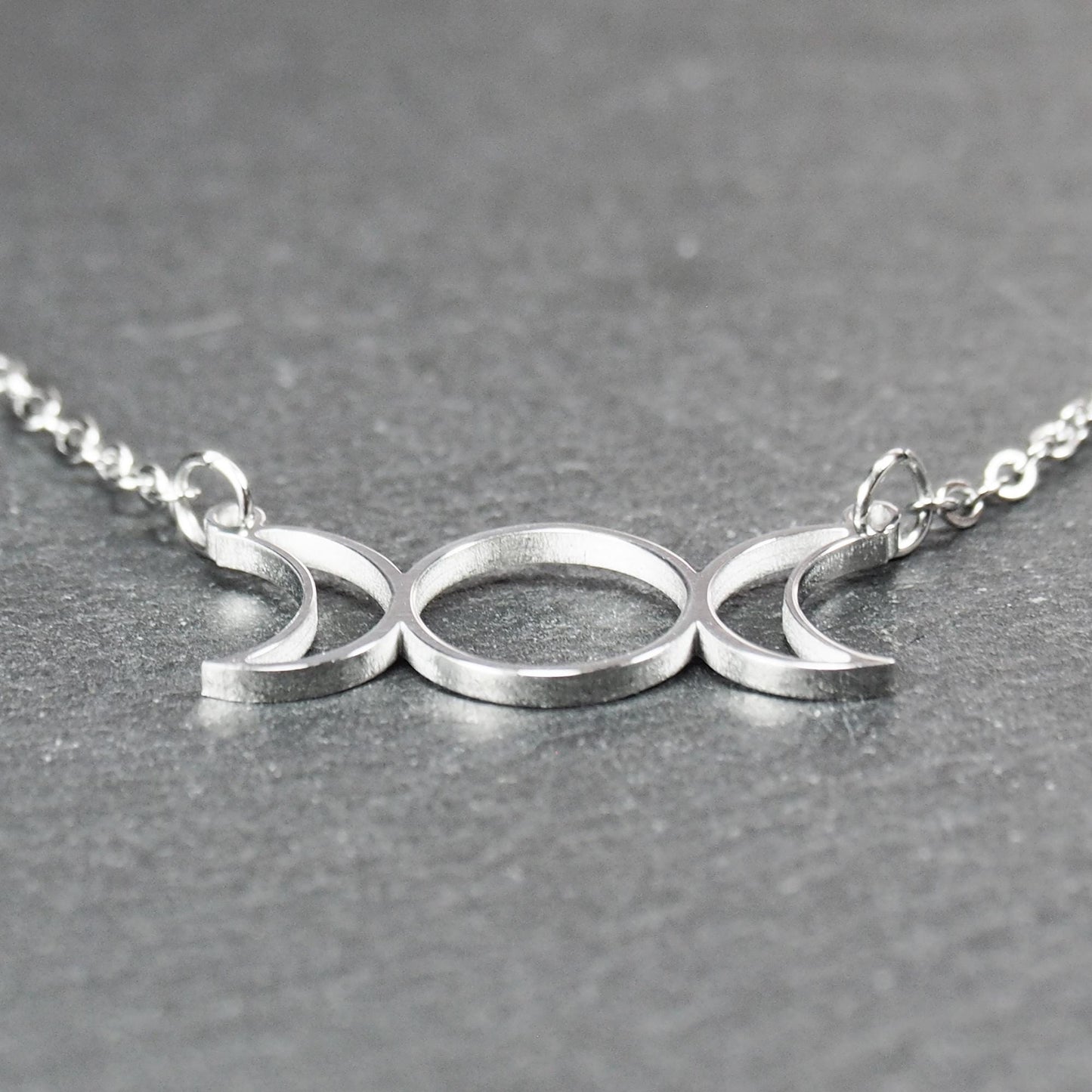 Filigranes silberfarbenes Collier mit offenem, symmetrischem Anhänger in Form dreier Mondphasen (zwei Mondsicheln neben Kreis) an Kette.