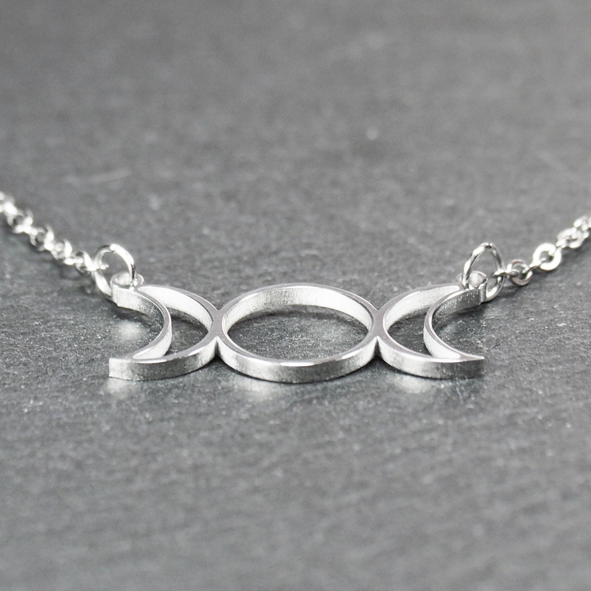 Filigranes silberfarbenes Collier mit offenem, symmetrischem Anhänger in Form dreier Mondphasen (zwei Mondsicheln neben Kreis) an Kette.