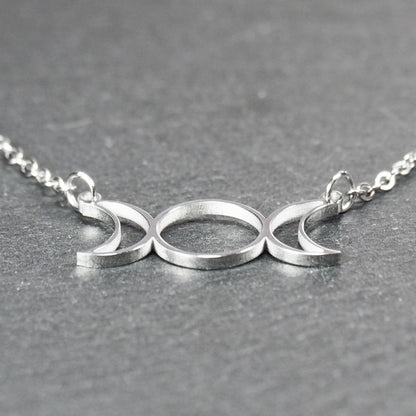 Filigranes silberfarbenes Collier mit offenem, symmetrischem Anhänger in Form dreier Mondphasen (zwei Mondsicheln neben Kreis) an Kette.
