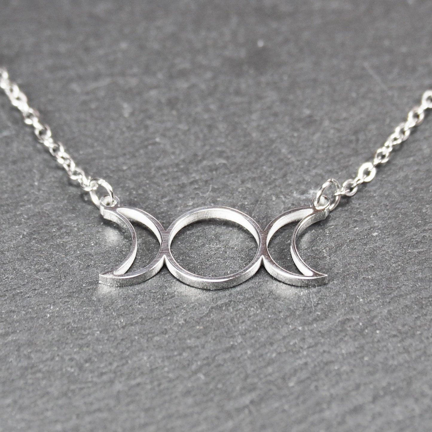 Filigranes silberfarbenes Collier mit offenem, symmetrischem Anhänger in Form dreier Mondphasen (zwei Mondsicheln neben Kreis) an Kette.