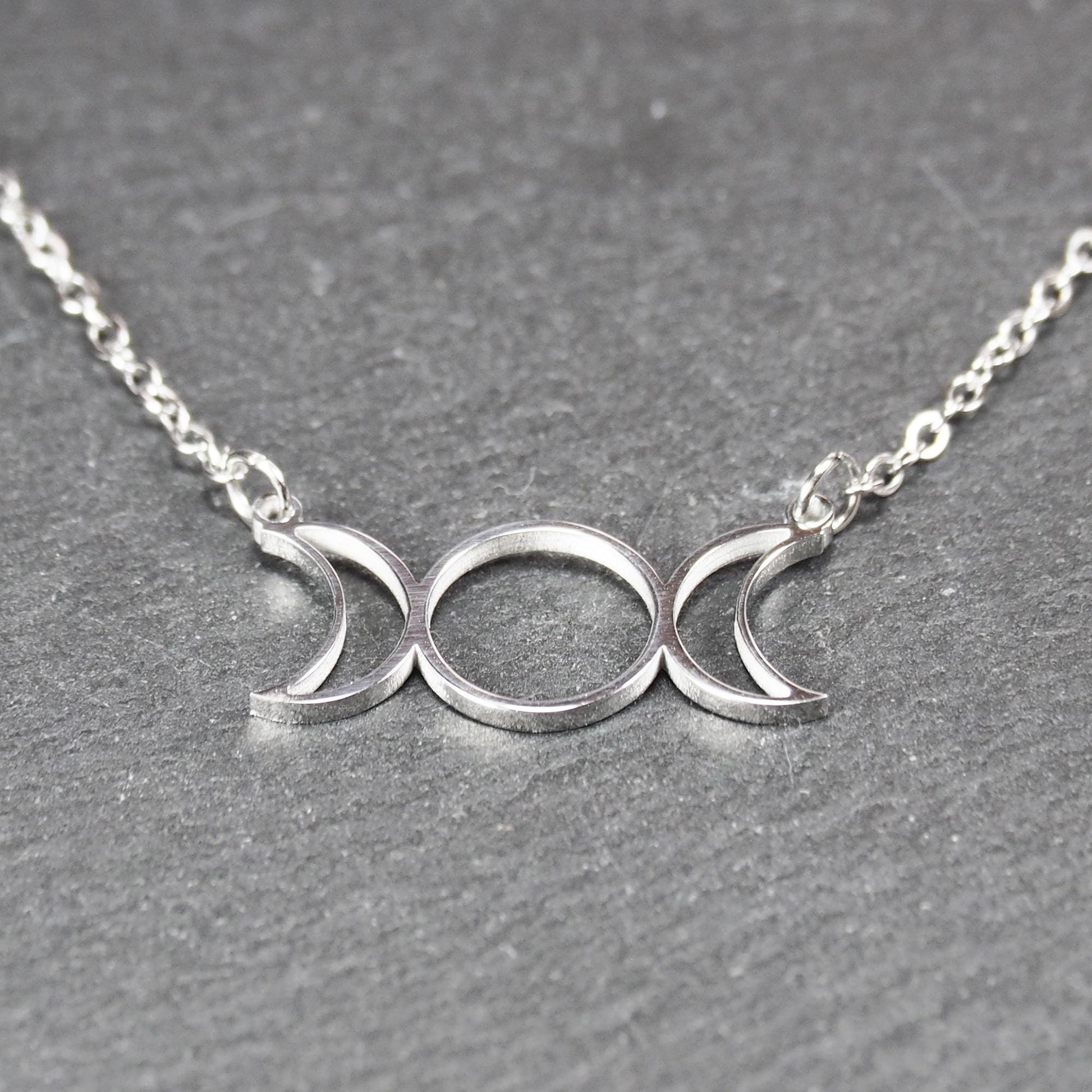 Filigranes silberfarbenes Collier mit offenem, symmetrischem Anhänger in Form dreier Mondphasen (zwei Mondsicheln neben Kreis) an Kette.
