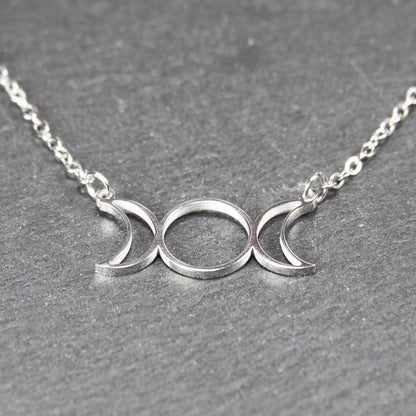 Filigranes silberfarbenes Collier mit offenem, symmetrischem Anhänger in Form dreier Mondphasen (zwei Mondsicheln neben Kreis) an Kette.