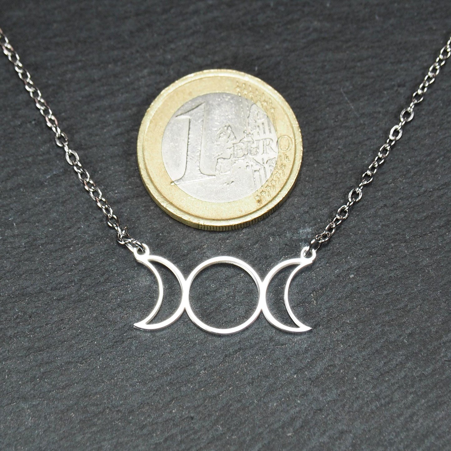Silberfarbenes Collier mit offenem, filigranem Drei‑Mond‑Anhänger (zwei Mondsicheln und Kreis); 1‑Euro‑Münze als Größenvergleich.