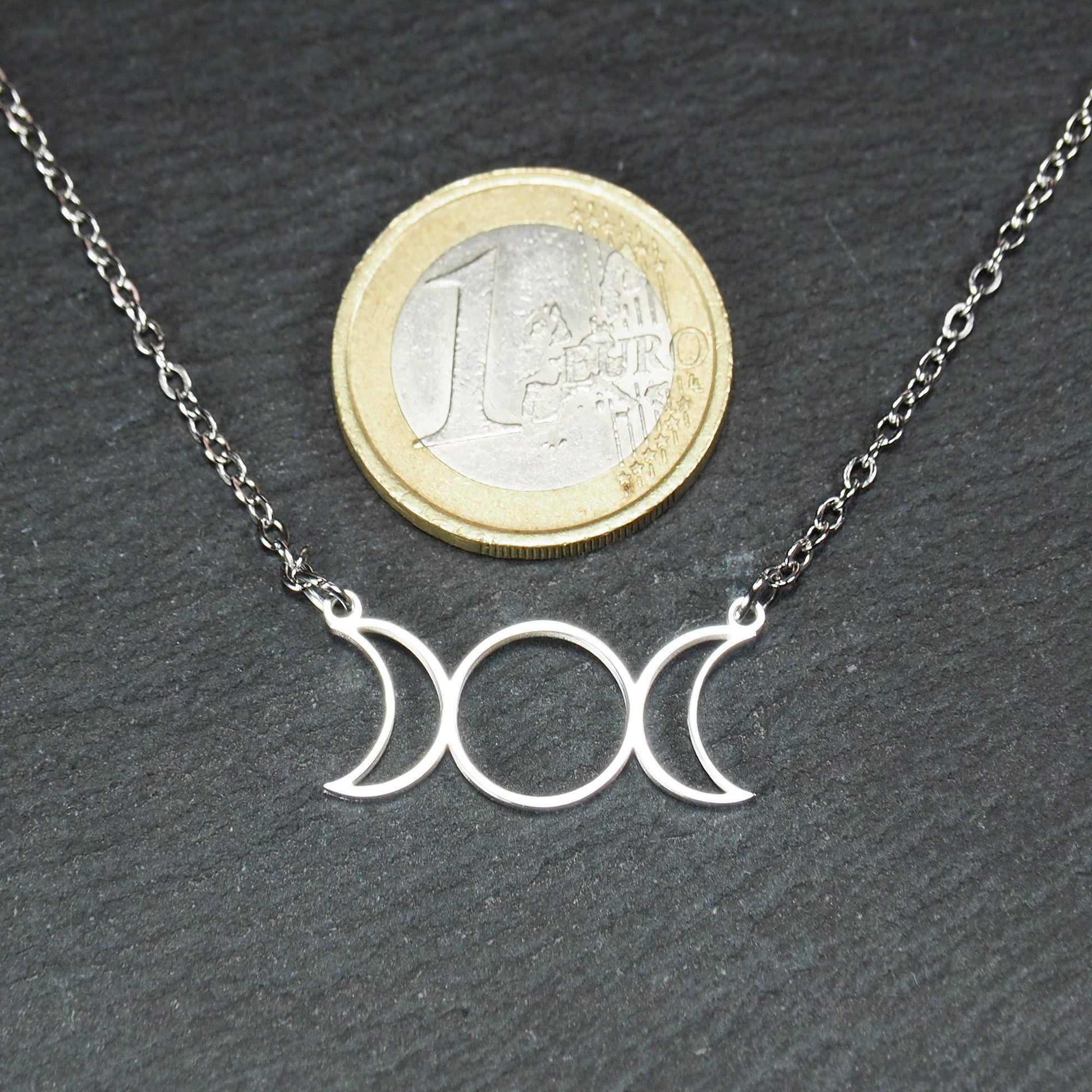 Silberfarbenes Collier mit offenem, filigranem Drei‑Mond‑Anhänger (zwei Mondsicheln und Kreis); 1‑Euro‑Münze als Größenvergleich.