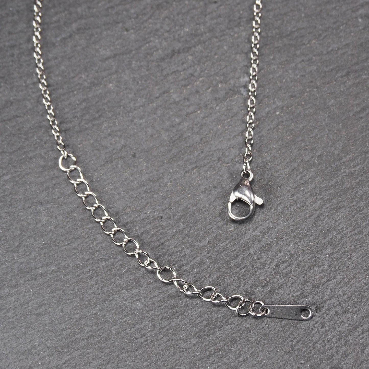 Versilberte Halskette mit feiner Gliederkette, Verlängerungskette mit ovalen Gliedern, Karabinerverschluss und flachem Endplättchen mit Loch.