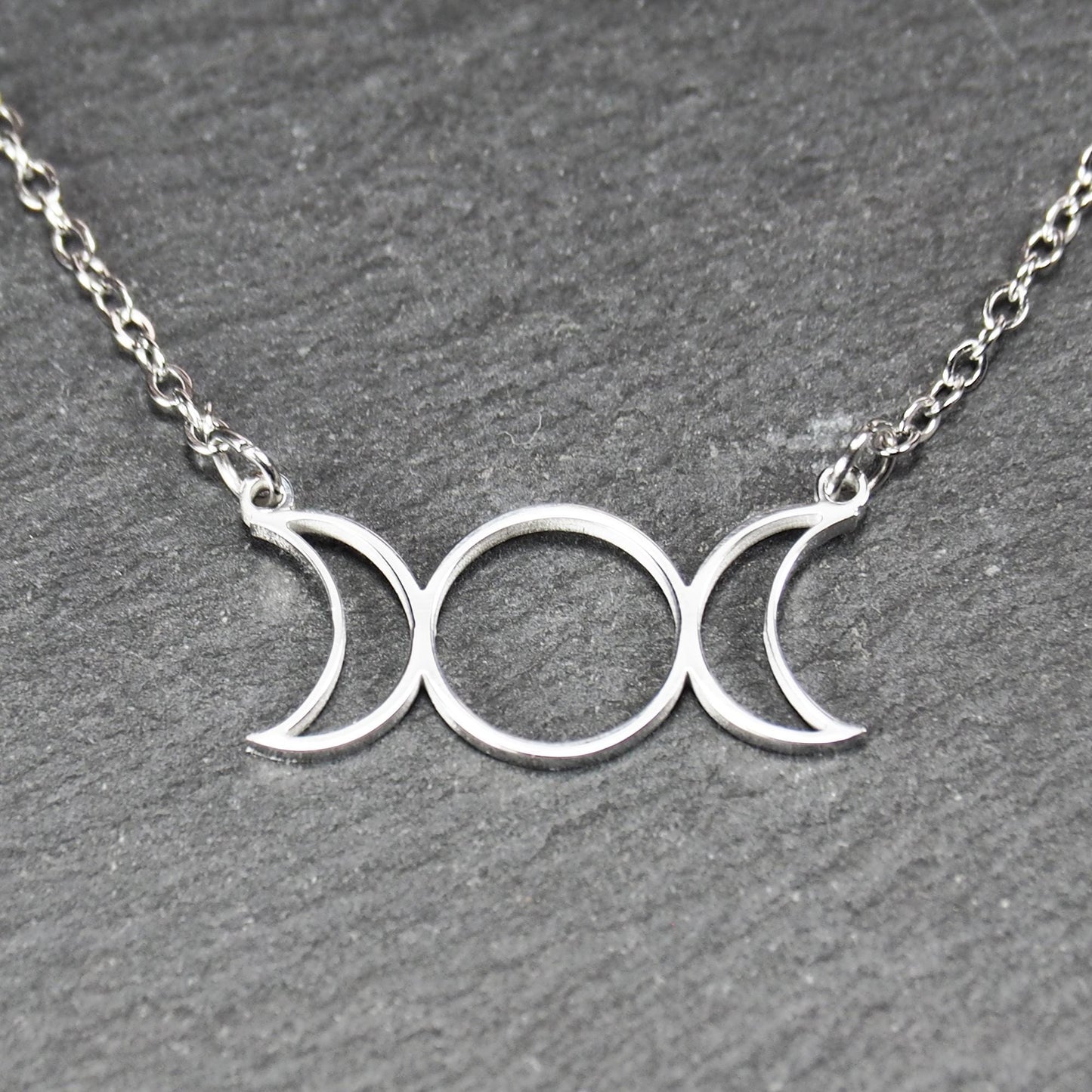 Filigranes silberfarbenes Collier mit offenem, symmetrischem Anhänger in Form dreier Mondphasen (zwei Mondsicheln neben Kreis) an Kette.