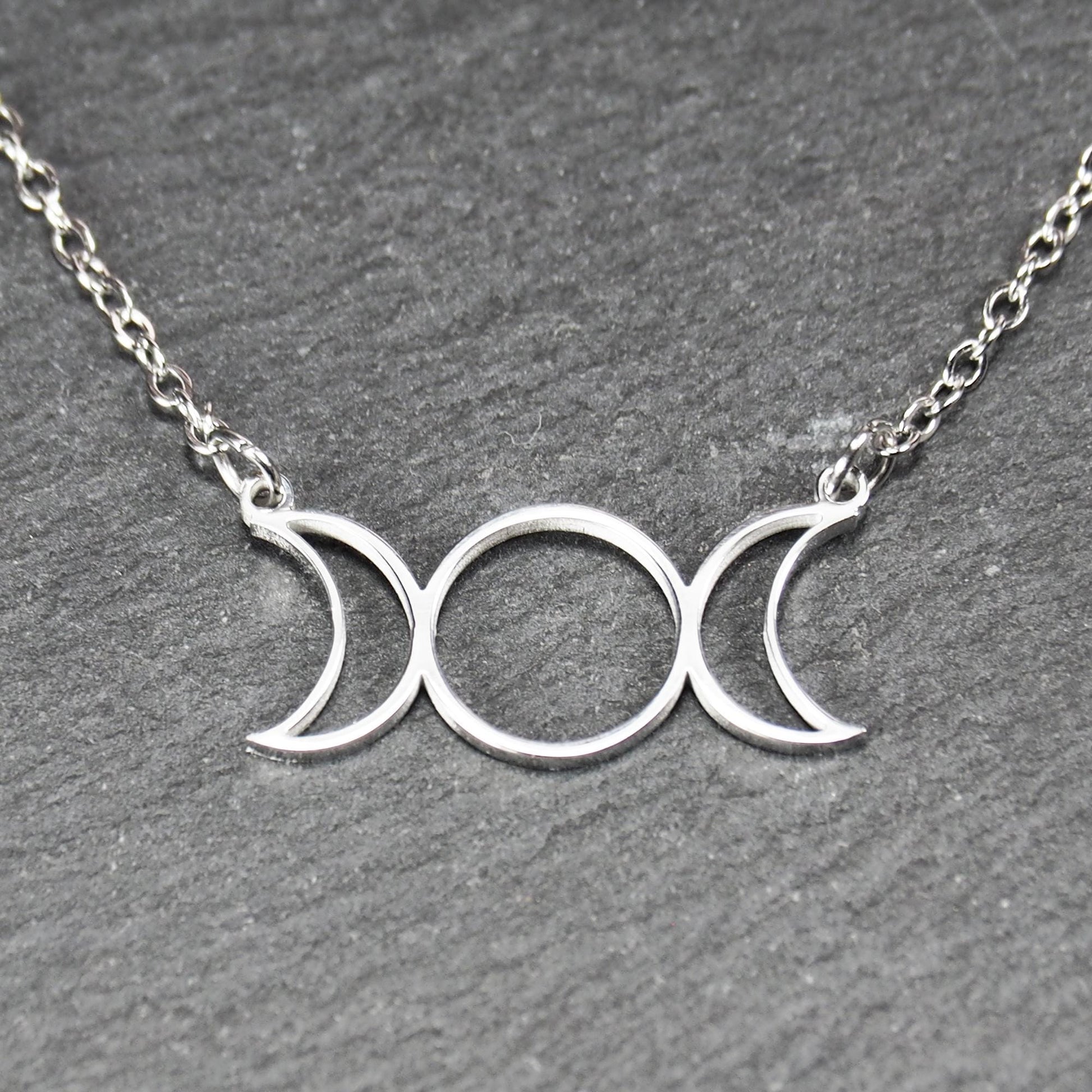 Filigranes silberfarbenes Collier mit offenem, symmetrischem Anhänger in Form dreier Mondphasen (zwei Mondsicheln neben Kreis) an Kette.