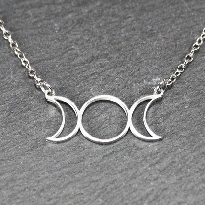 Filigranes silberfarbenes Collier mit offenem, symmetrischem Anhänger in Form dreier Mondphasen (zwei Mondsicheln neben Kreis) an Kette.