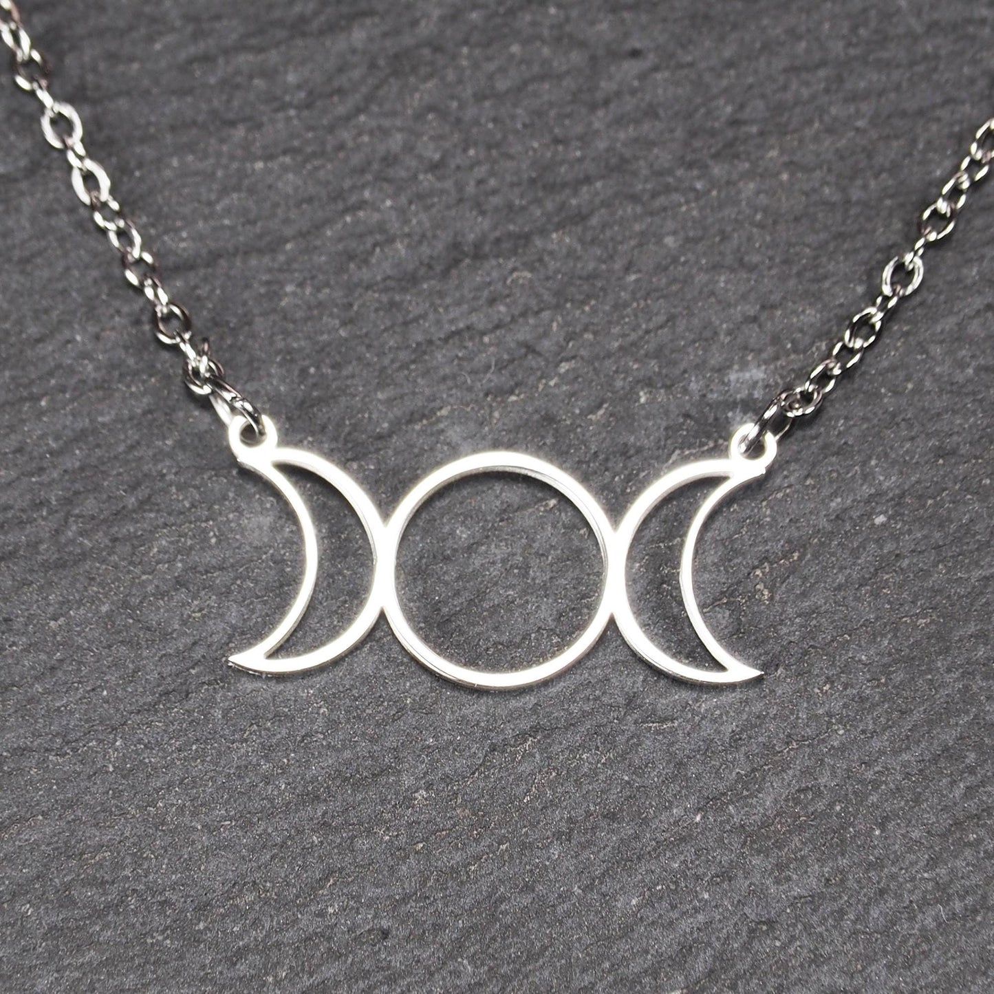 Filigranes silberfarbenes Collier mit offenem, symmetrischem Anhänger in Form dreier Mondphasen (zwei Mondsicheln neben Kreis) an Kette.