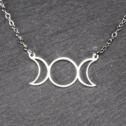 Filigranes silberfarbenes Collier mit offenem, symmetrischem Anhänger in Form dreier Mondphasen (zwei Mondsicheln neben Kreis) an Kette.