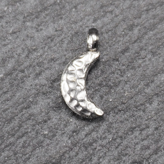 Halbmond-Anhänger, silberfarben metallisch mit gehämmerter, reliefartiger Oberfläche und integrierter Öse oben.