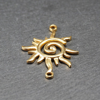 Goldfarbener, durchbrochener Sonnen-Verbinder mit spiralförmigem Zentrum, unregelmäßigen wellenförmigen Strahlen und je einer Öse oben und unten.