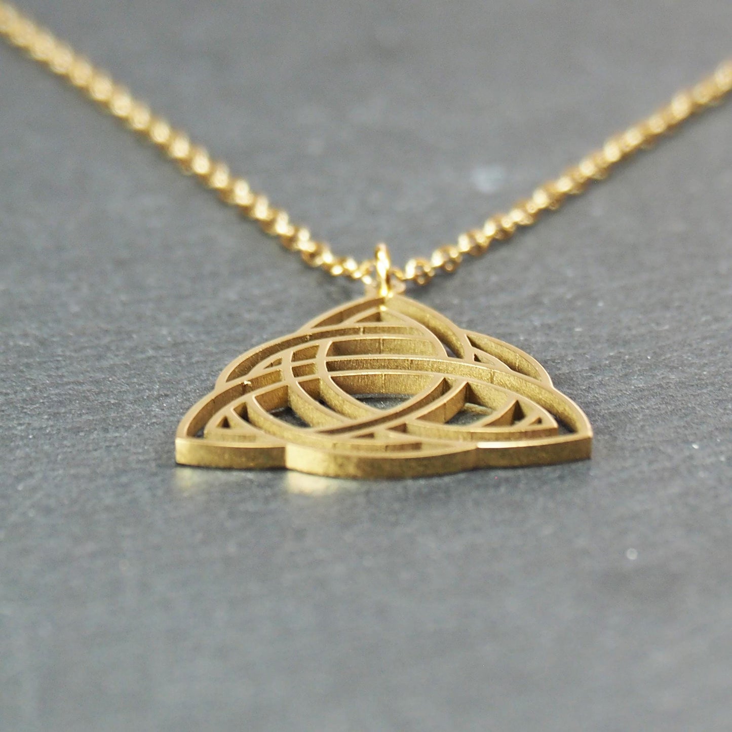 Vergoldeter Anhänger in offener Triquetra-Knotenform mit filigranen Durchbrüchen, an dünner goldfarbener Kette und sichtbarer Öse.