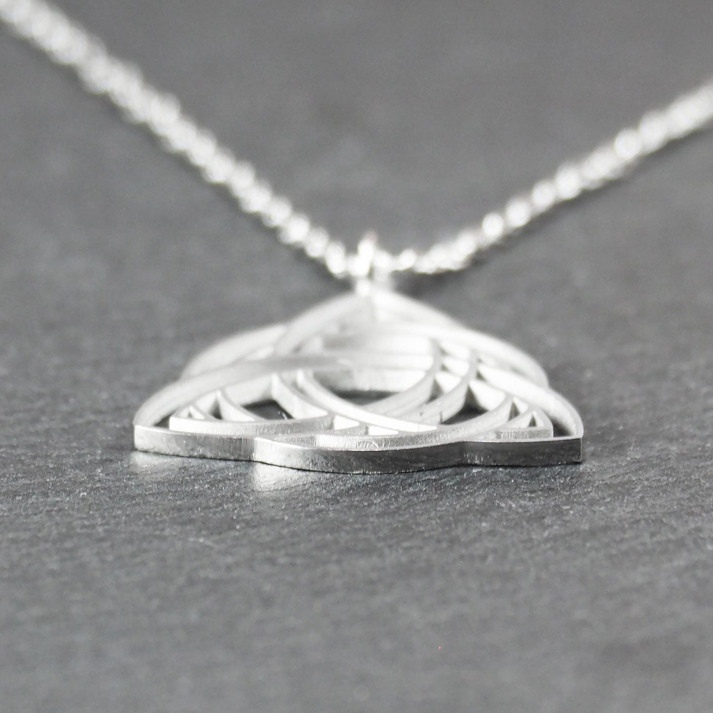 Anhänger, silberfarben glänzend; dreieckige, offene Triquetra-Knotenform mit filigraner Durchbruchstruktur und sichtbarer Öse an feiner Gliederkette.