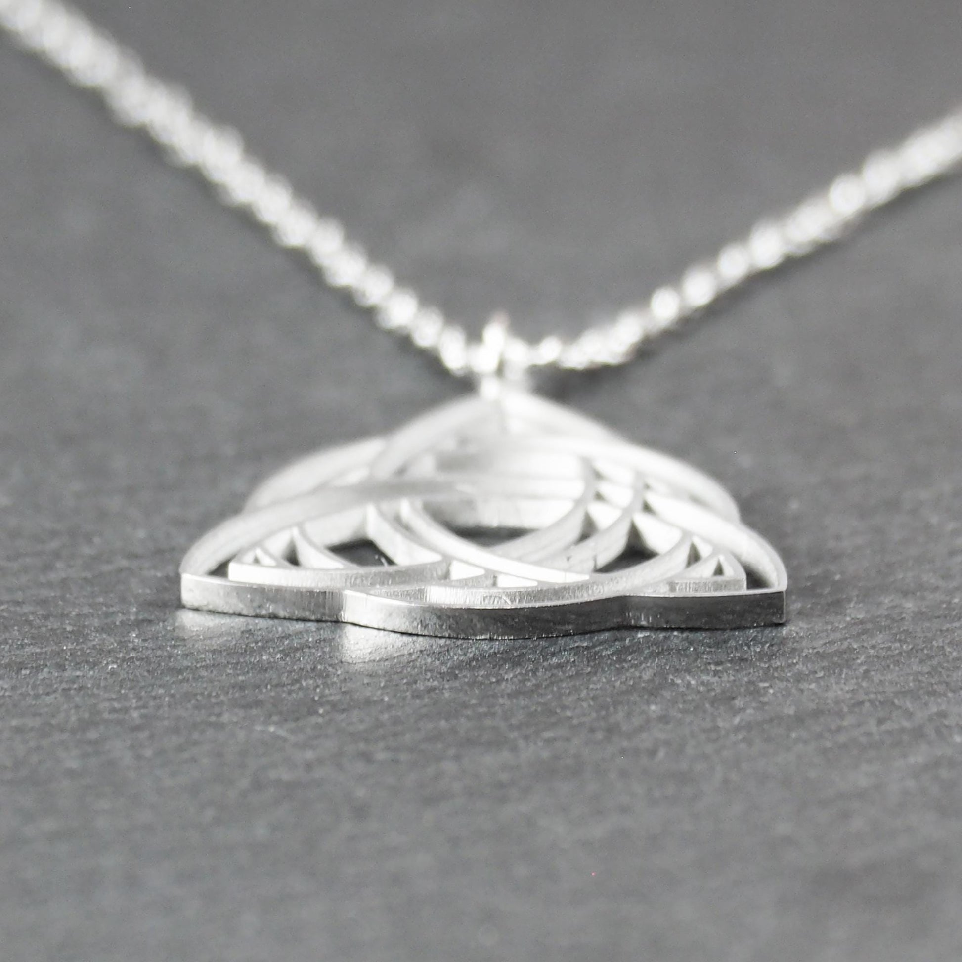 Anhänger, silberfarben glänzend; dreieckige, offene Triquetra-Knotenform mit filigraner Durchbruchstruktur und sichtbarer Öse an feiner Gliederkette.