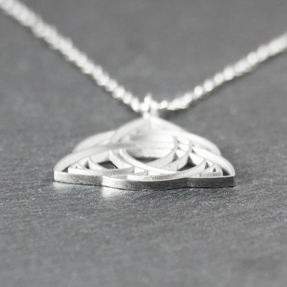 Anhänger, silberfarben glänzend; dreieckige, offene Triquetra-Knotenform mit filigraner Durchbruchstruktur und sichtbarer Öse an feiner Gliederkette.