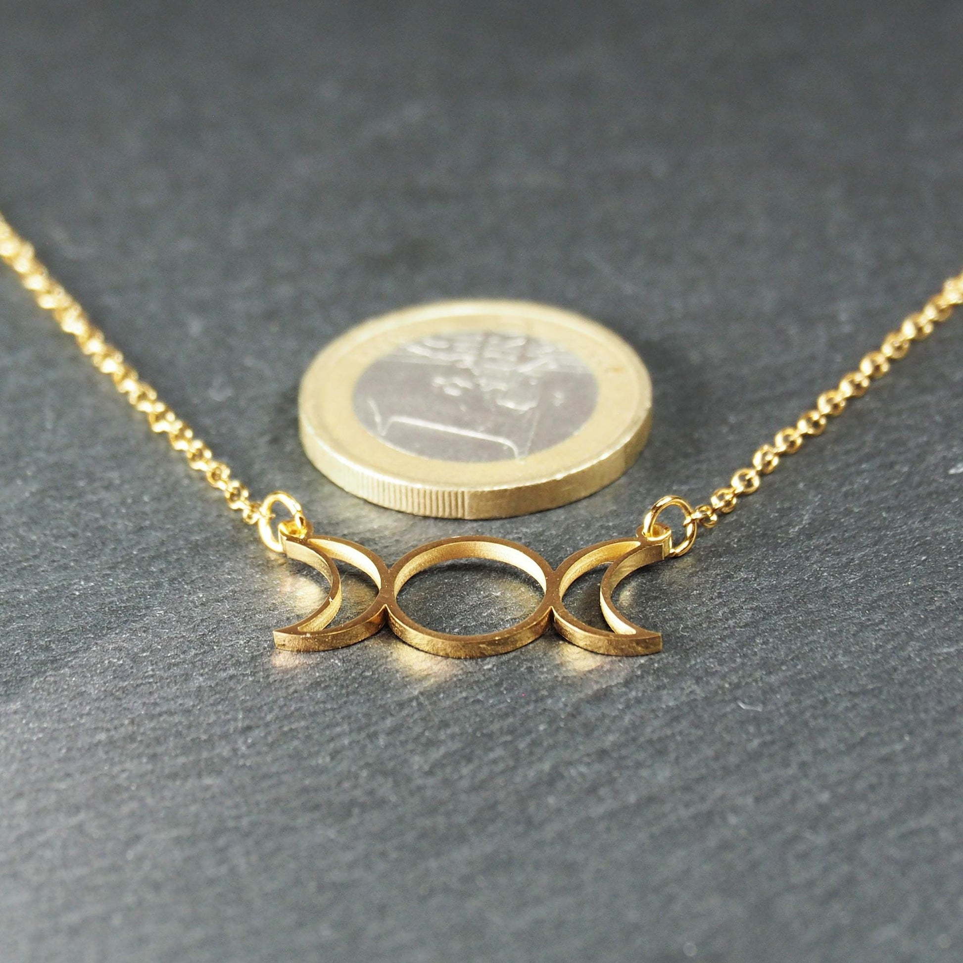 Collier mit goldfarbener Kette und offenem, durchbrochenem Anhänger in Form der dreifachen Mondgöttin mit Ösen; Ein-Euro-Münze als Größenvergleich.