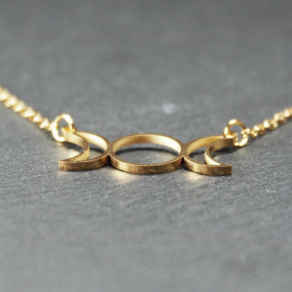 Collier mit goldfarbenem, offenem Anhänger in dreifacher Mondform (Mondsichel-Kreis-Mondsichel), an einer feinen Gliederkette mittels Ösen befestigt.