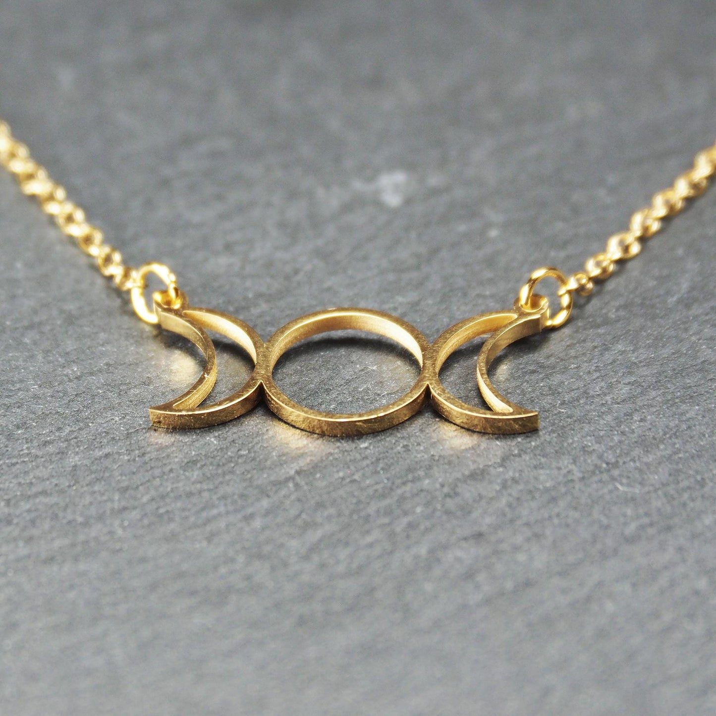 Collier mit goldfarbenem, offenem Anhänger in dreifacher Mondform (Mondsichel-Kreis-Mondsichel), an einer feinen Gliederkette mittels Ösen befestigt.