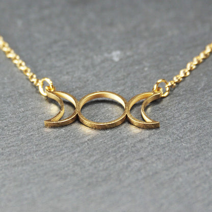 Collier mit goldfarbenem, offenem Anhänger in dreifacher Mondform (Mondsichel-Kreis-Mondsichel), an einer feinen Gliederkette mittels Ösen befestigt.
