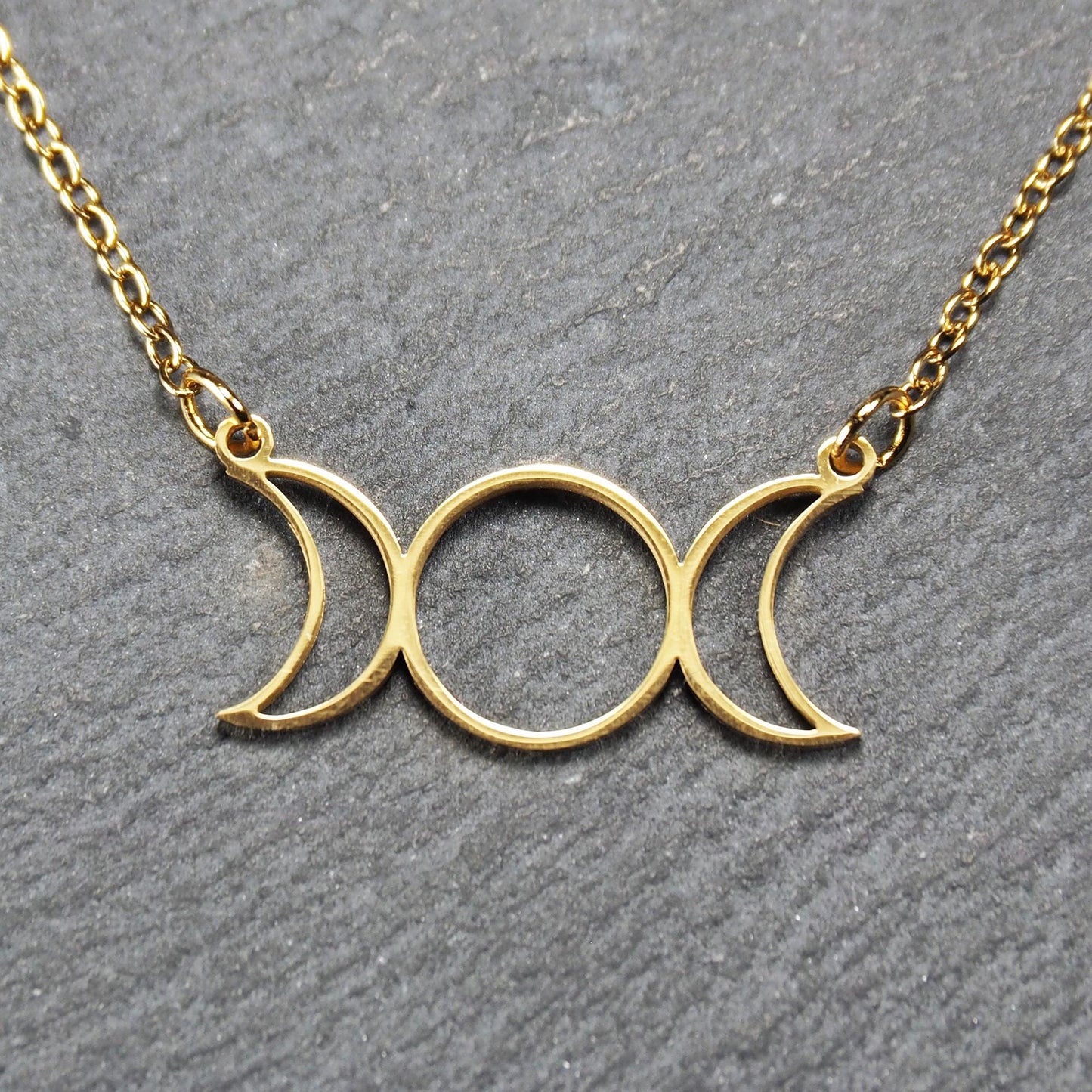 Collier mit goldfarbenem, offenem Anhänger in dreifacher Mondform (Mondsichel-Kreis-Mondsichel), an einer feinen Gliederkette mittels Ösen befestigt.