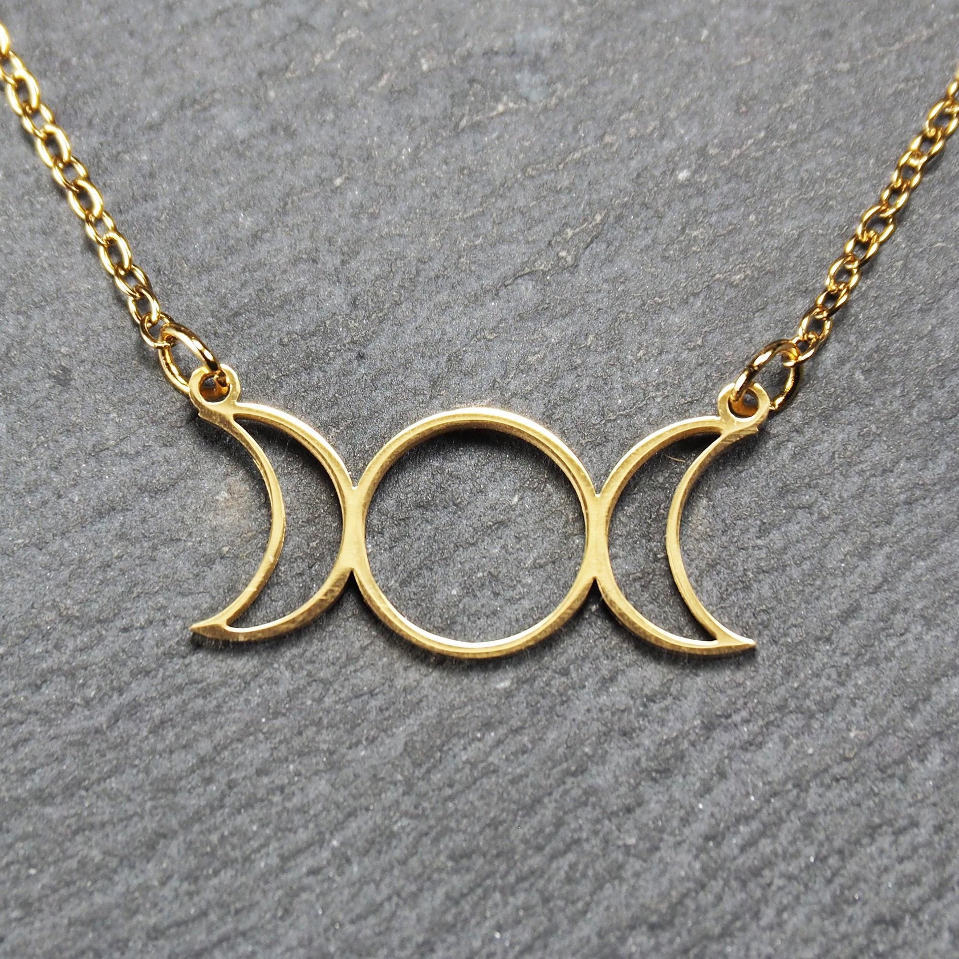 Collier mit goldfarbenem, offenem Anhänger in dreifacher Mondform (Mondsichel-Kreis-Mondsichel), an einer feinen Gliederkette mittels Ösen befestigt.