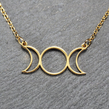 Collier mit goldfarbenem, offenem Anhänger in dreifacher Mondform (Mondsichel-Kreis-Mondsichel), an einer feinen Gliederkette mittels Ösen befestigt.