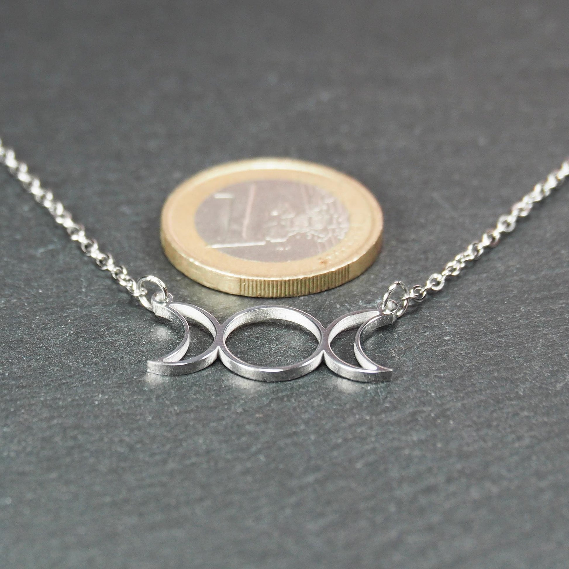 Silberfarbenes Collier mit offenem, filigranem Drei‑Mond‑Anhänger (zwei Mondsicheln und Kreis); 1‑Euro‑Münze als Größenvergleich.