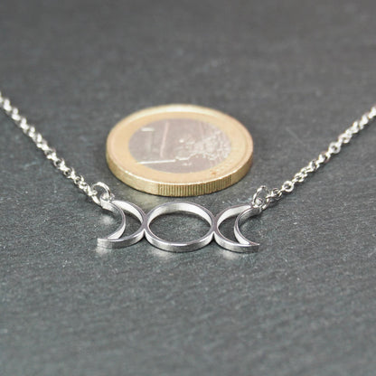 Silberfarbenes Collier mit offenem, filigranem Drei‑Mond‑Anhänger (zwei Mondsicheln und Kreis); 1‑Euro‑Münze als Größenvergleich.